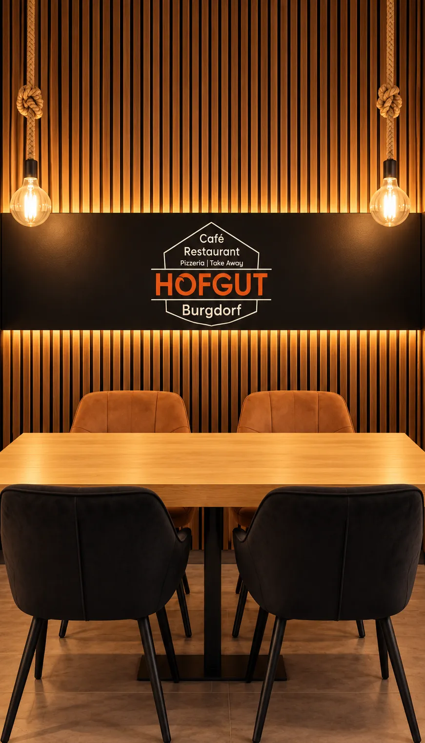 Tisch im Hofgut vor der beleuchteten Holzwand mit Hofgut-Logo